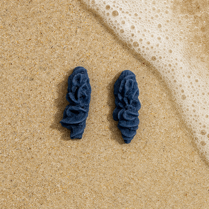 Pair of deep cobalt blue porcelain coral earrings on sand by the sea.