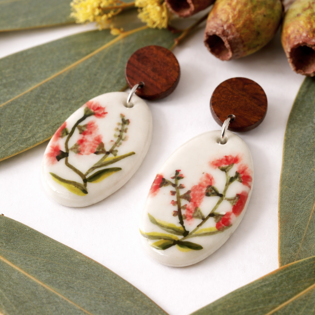 Hand-painted porcelain dangle earrings featuring a bursting gumnut design with wooden stud tops on a scene