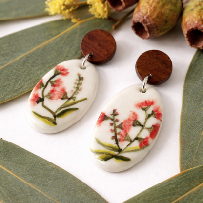 Hand-painted porcelain dangle earrings featuring a bursting gumnut design with wooden stud tops on a scene