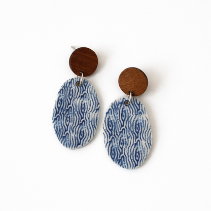 Handmade oval porcelain dangle earrings with blue and white sea-inspired pattern and wooden studs on a white background