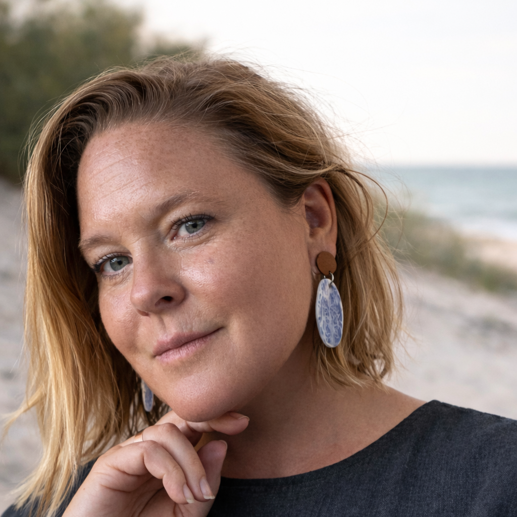 Woman wearing handmade oval porcelain dangle earrings with blue and white ocean pattern and wooden studs